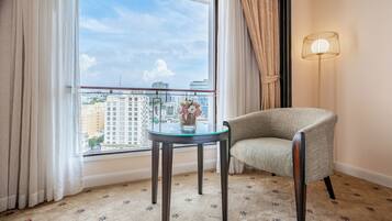 A room with a view of a cityscape, a round glass table, a cushioned armchair, and a floor lamp.