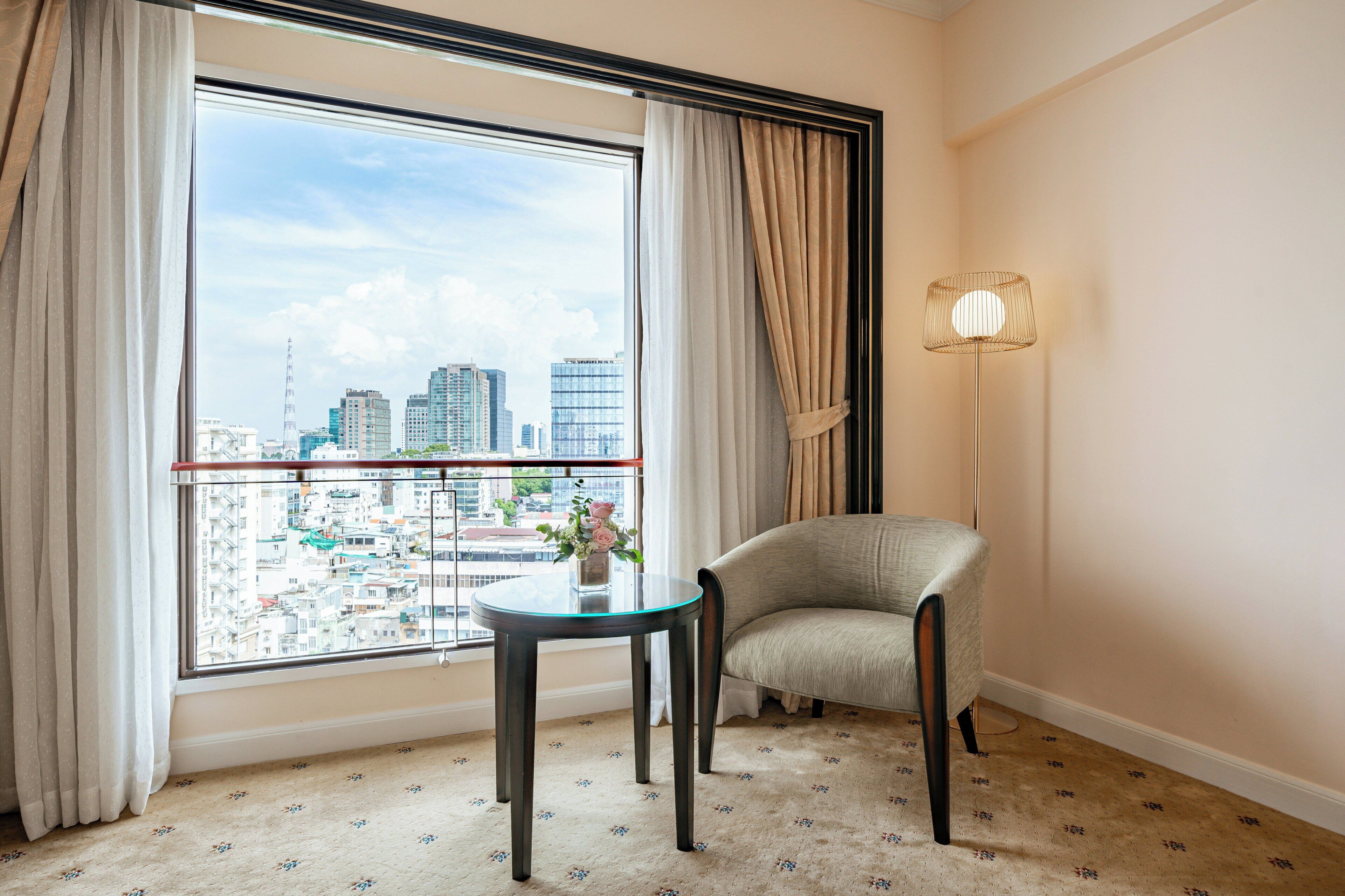 A room with a view of a cityscape, a round table, a chair, and a floor lamp.