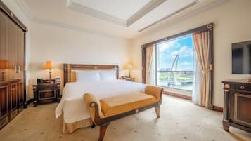 A hotel room with a large bed, a bench, a TV, and a view of a bridge.