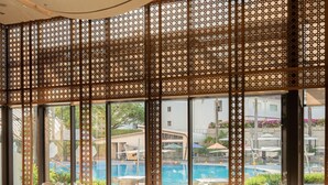 A restaurant with outdoor seating, large windows, and a view of a swimming pool. - Lotte Hotel Saigon (Ho Chi Minh City)