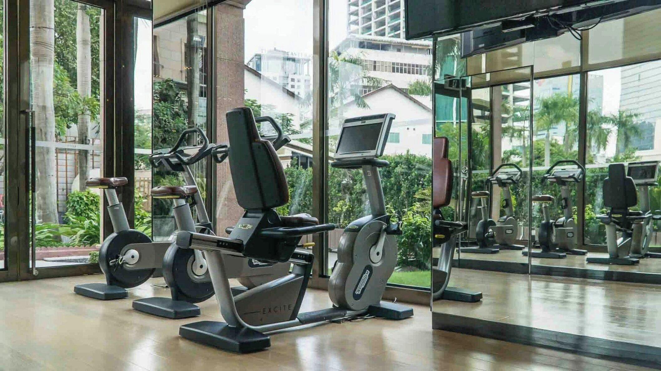 A gym with exercise equipment, large windows, and a view of buildings and trees.