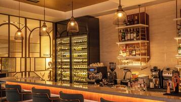 Una zona de bar con mostrador, taburetes, un enfriador de vino y una variedad de botellas y copas.