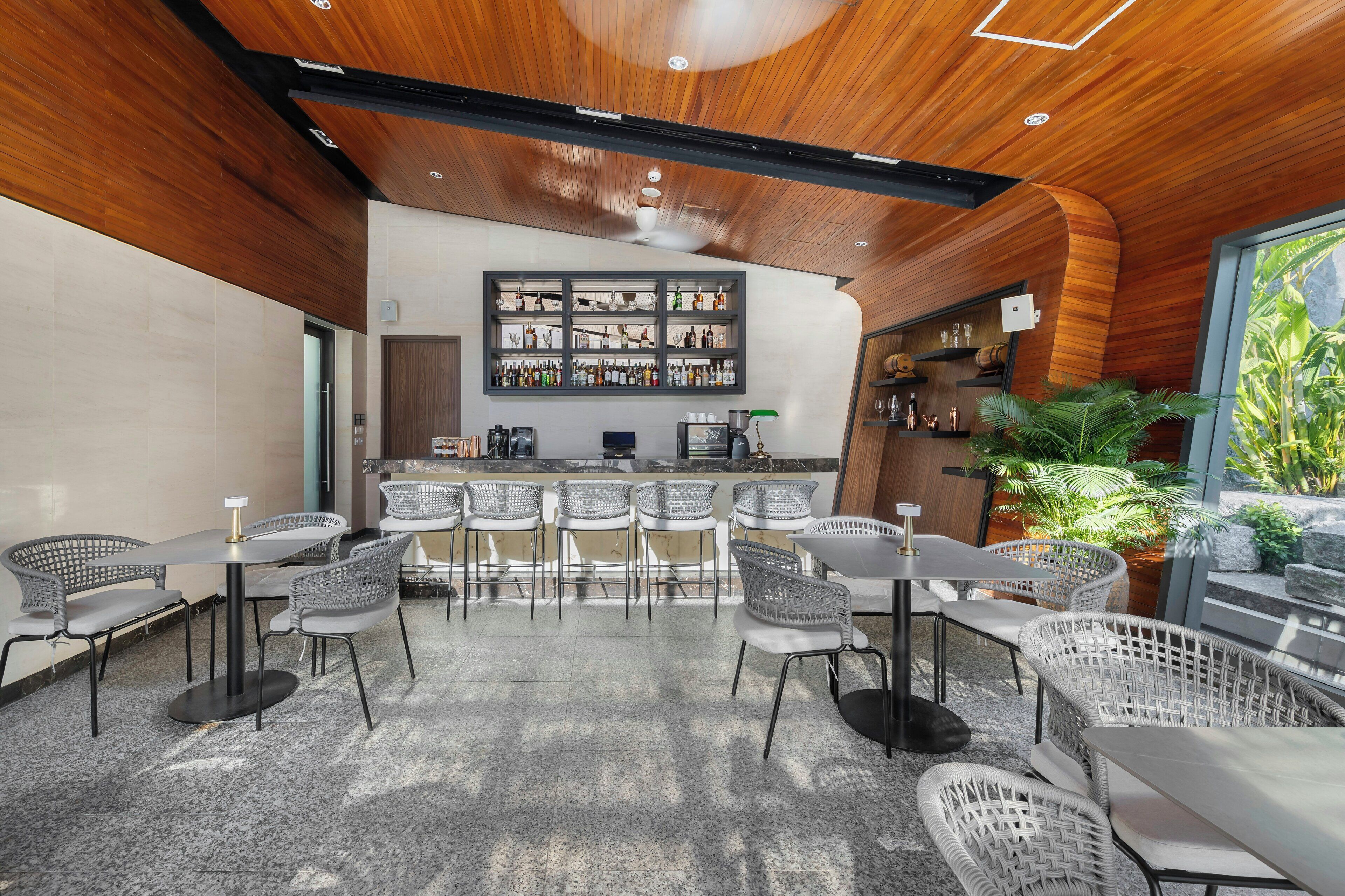 Zona de bar moderna con techo de madera, taburetes y una exhibición de botellas.