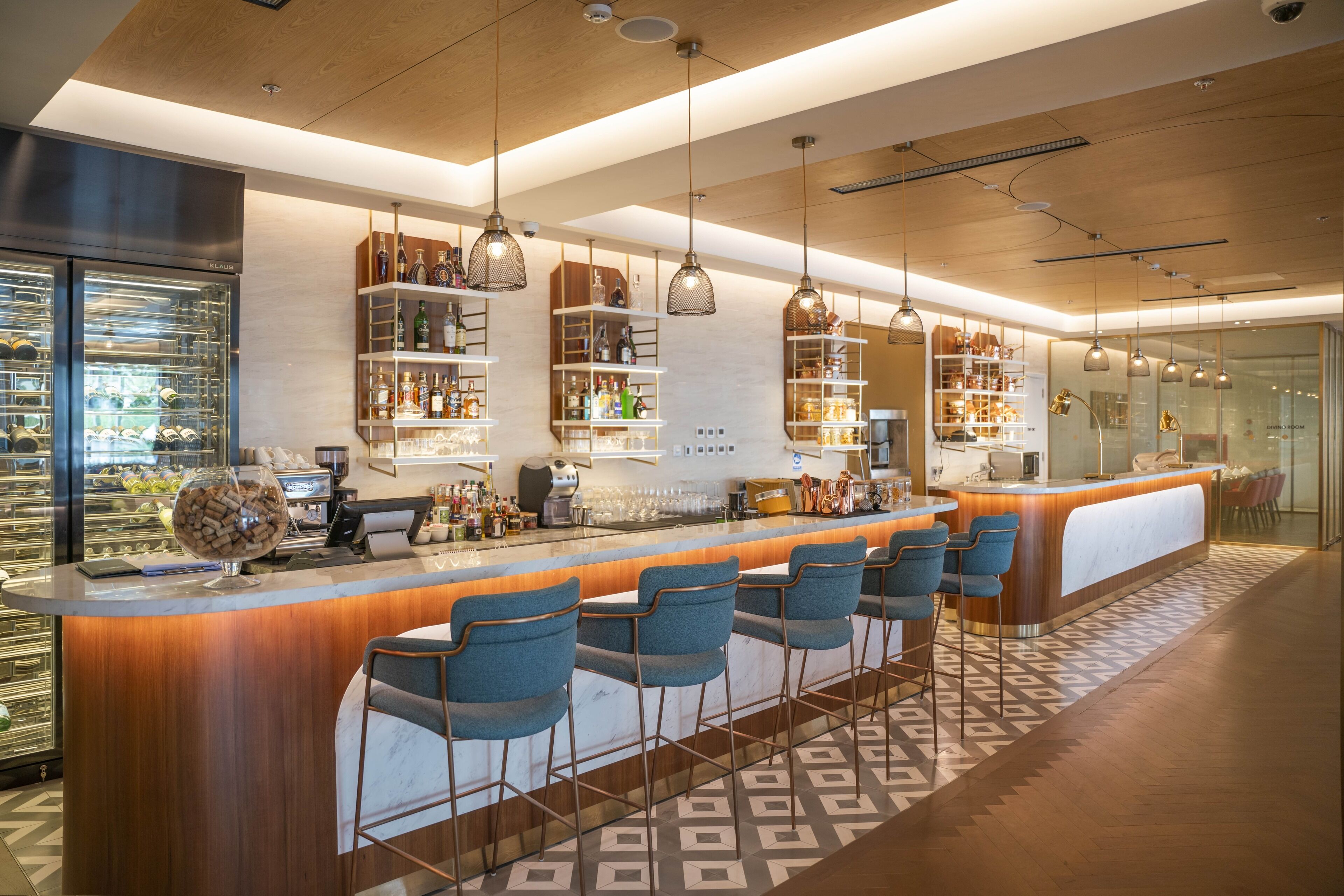 A modern bar area with a wooden counter, bar stools, and overhead pendant lighting.