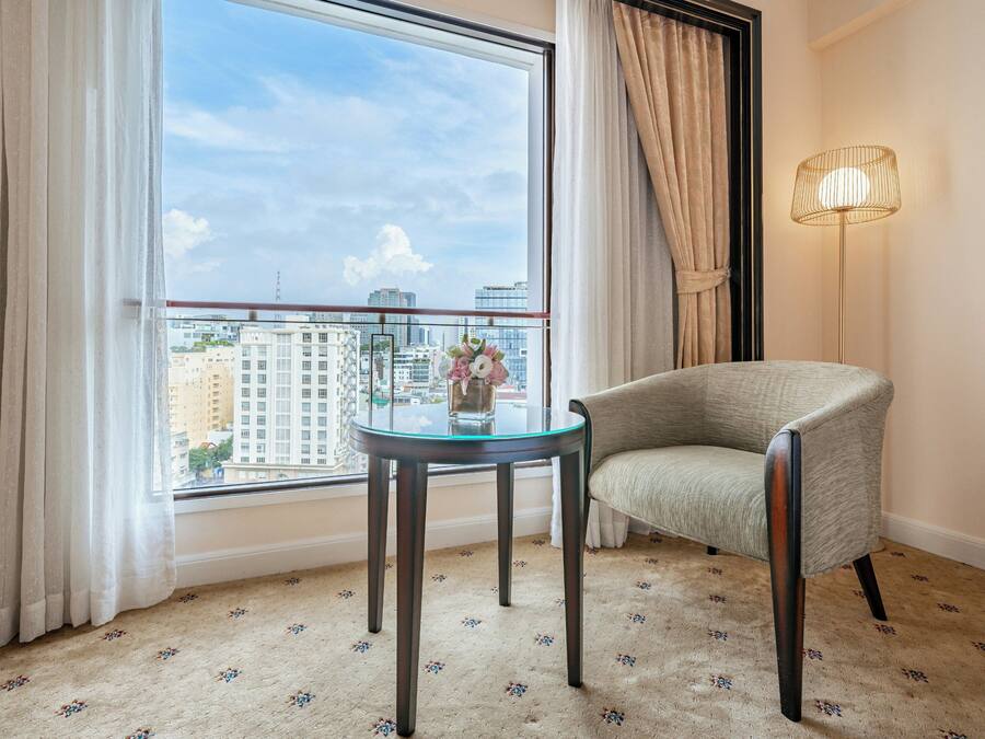 A room with a view of a cityscape, a round glass table, a chair, and a floor lamp.