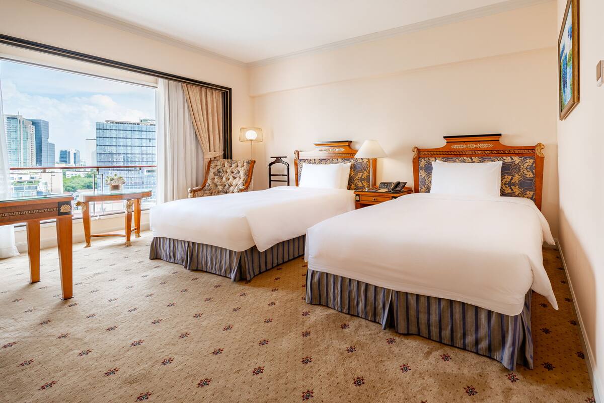 Hotellihuone, jossa on kaksi sänkyä, työpöytä, tuoli ja näkymä kaupunkiin.