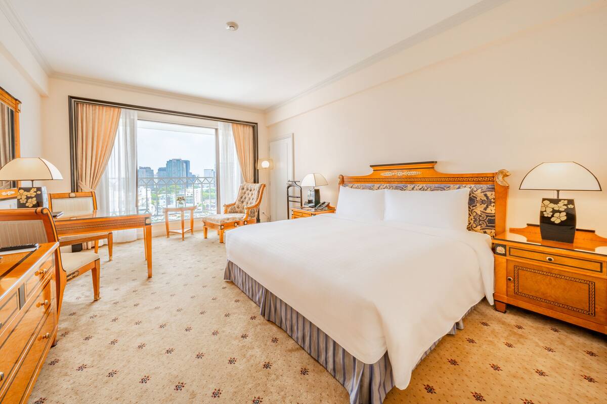 Hotellihuone, jossa on suuri sänky, työpöytä, tuoli, yöpöytä ja ikkunasta avautuva näkymä kaupunkiin.