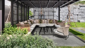 A covered outdoor seating area with a modern design, featuring a sectional sofa, round tables, and wicker chairs. - Lotte Hotel Saigon (Ho Chi Minh City)