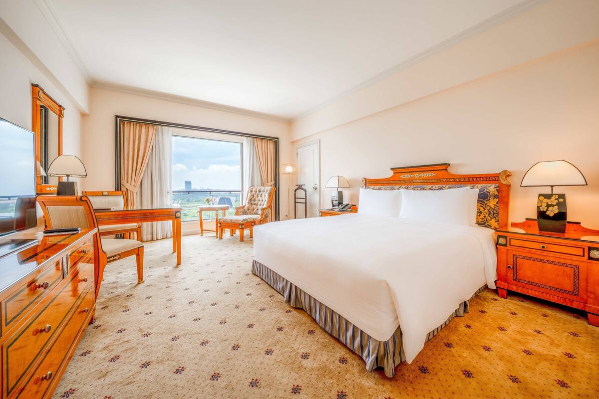 Hotellihuone, jossa on suuri sänky, työpöytä, tuoli ja näkymä kaupunkiin.