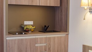 Een kleine keuken met houten kastjes, een zwarte spoelbak en een fruitschaal op het aanrecht.