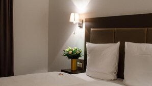 Een hotelkamer met een bed, nachtkastje, lamp en een vaas met bloemen.