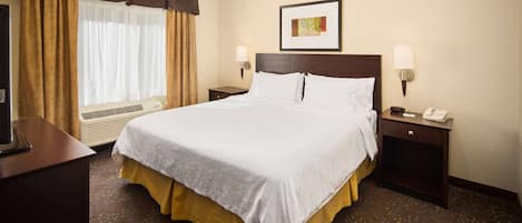 A hotel room with a large bed, two bedside tables, a desk, a chair, a window with curtains, and a wall-mounted picture.
