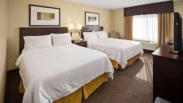 Quarto de hotel com duas camas, uma escrivaninha, uma cadeira e uma televisão.