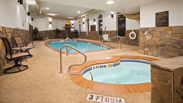 Une piscine intérieure avec un mur en pierre et un jacuzzi, entourée d’espaces aménagés pour s’asseoir.
