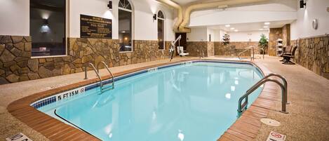 A pool area with a 5 FT 15M depth sign, a no diving sign, and a lifeguard on duty sign.