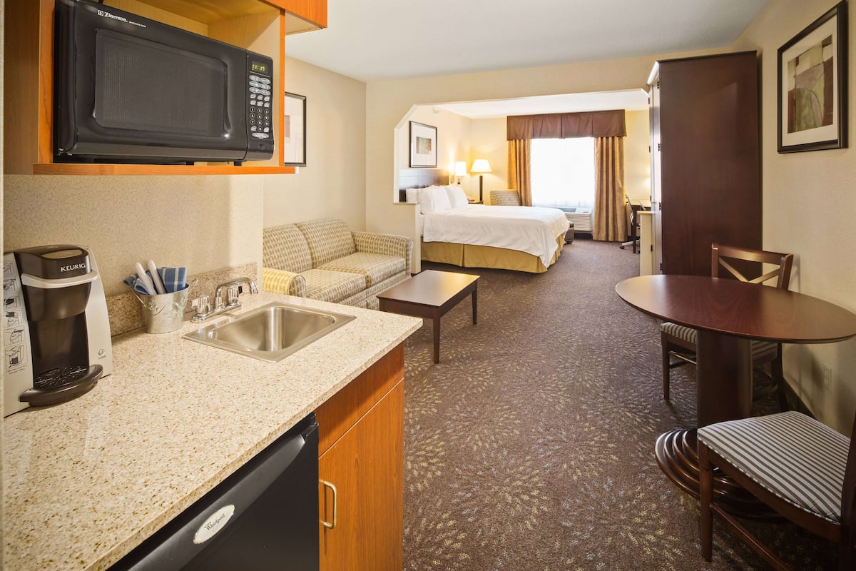 Una habitación de hotel con kitchenette, una cama, un escritorio y un área de comedor.