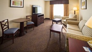 Une chambre d’hôtel avec une table ronde, deux chaises, un canapé, un téléviseur posé sur une commode et une lampe.
