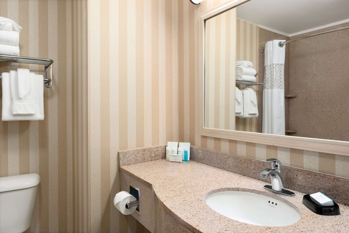 Une salle de bain avec un papier peint à rayures, un lavabo, un miroir et un porte-serviettes.
