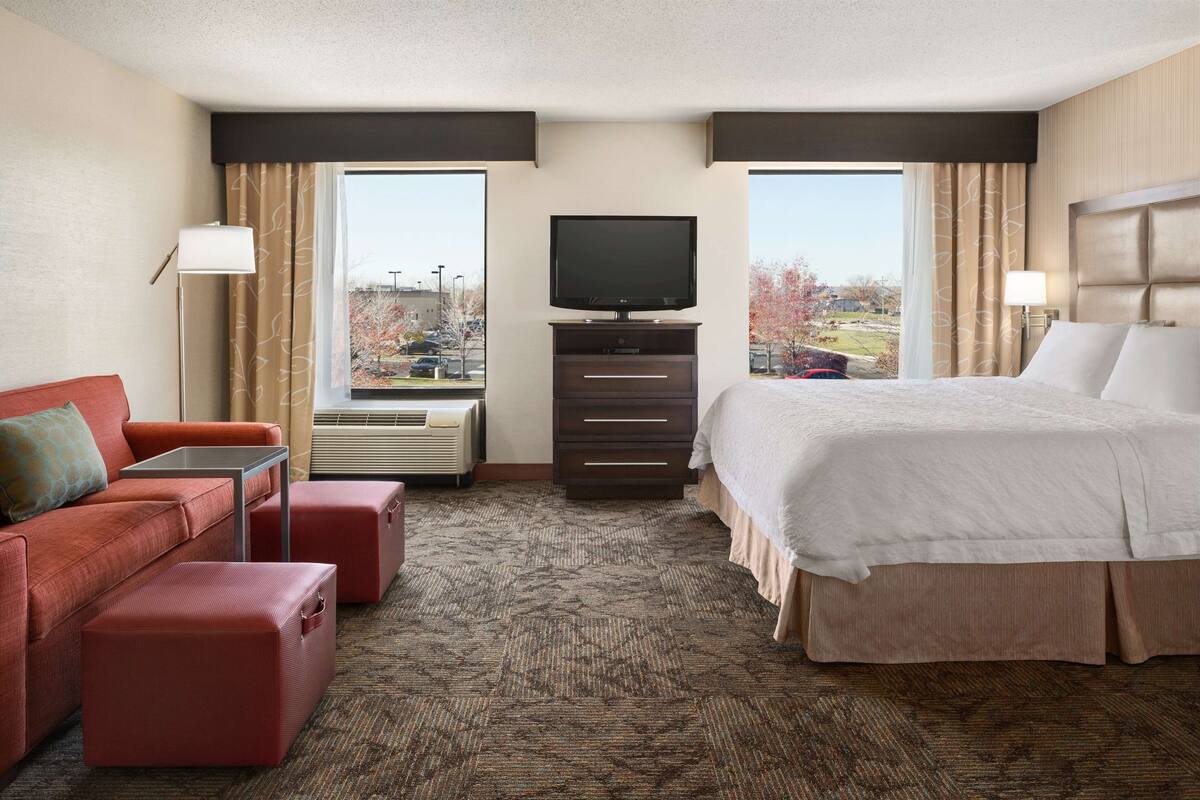 A hotel room with a bed, a sofa, a TV, and a window with a view of the outside.