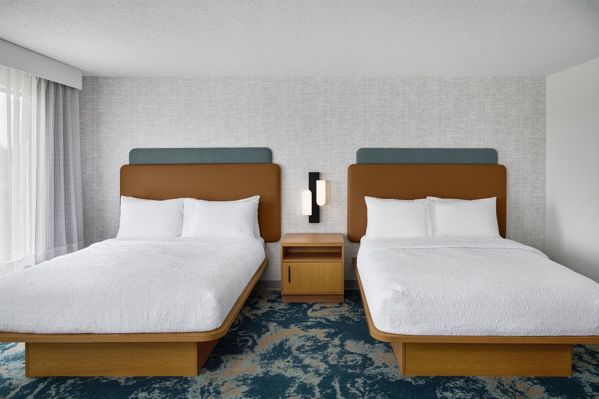 A hotel room with two beds, a nightstand, and a wall-mounted lamp.