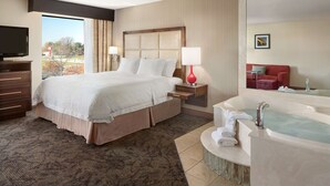 A hotel room with a large bed, a TV, a bathroom with a bathtub, and a red couch. - Hampton Inn & Suites Detroit/Sterling Heights (Sterling Heights)