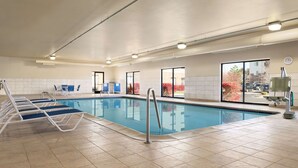 An indoor swimming pool with lounge chairs, a sun lounger, and a view of the outside through large windows. - Hampton Inn & Suites Detroit/Sterling Heights (Sterling Heights)