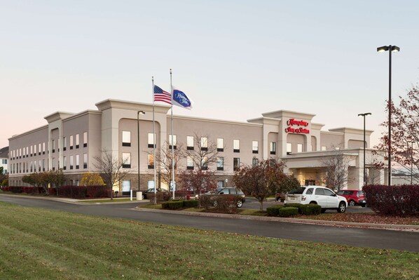 A Hampton Inn hotel with a flag, parking area, and a well-maintained lawn.