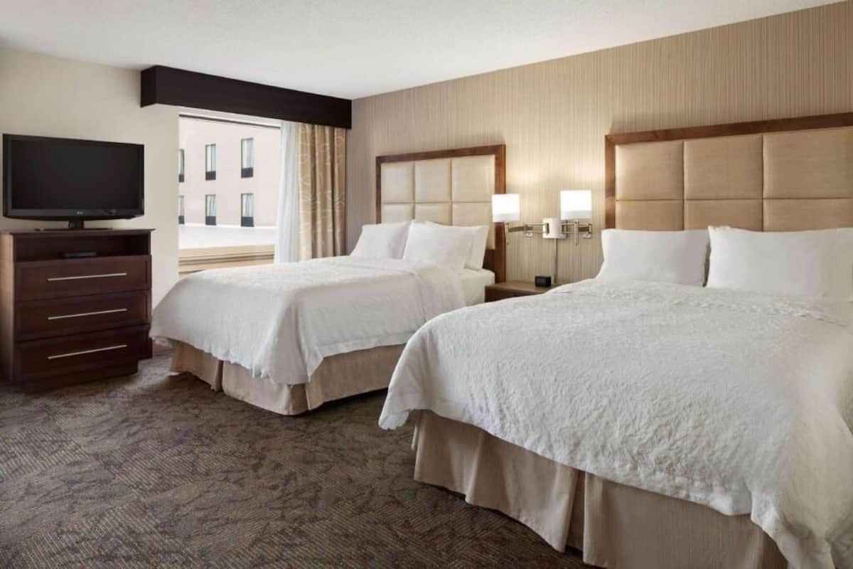 Une chambre d’hôtel avec deux lits, une télévision, une commode et une vue sur les bâtiments environnants.