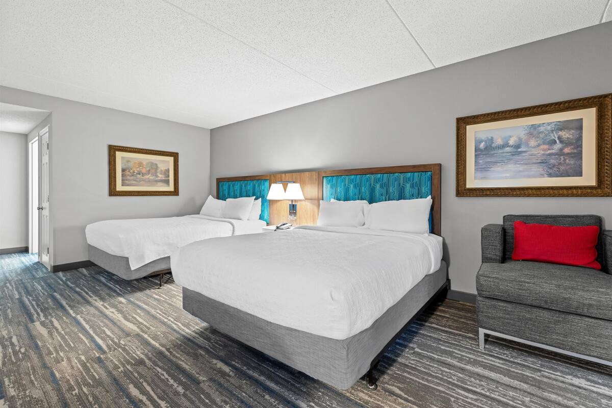 A hotel room with two beds, a sofa, and a painting on the wall.