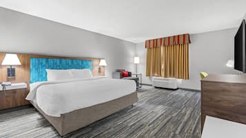 A hotel room with a bed, bedside tables, a desk, a chair, a TV, and a window with curtains.