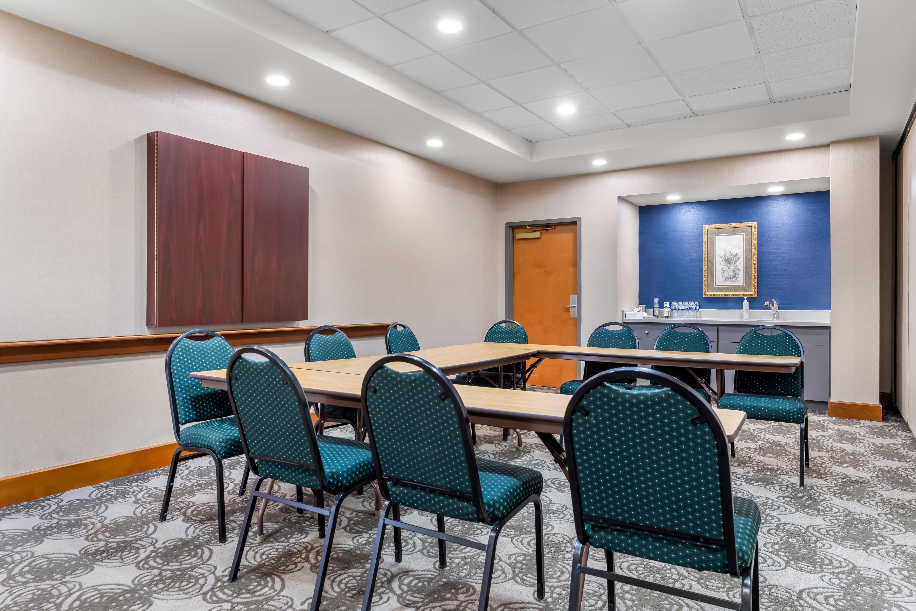 A conference room with a long table, multiple chairs, a wooden cabinet, a door, and a wall with a framed picture.