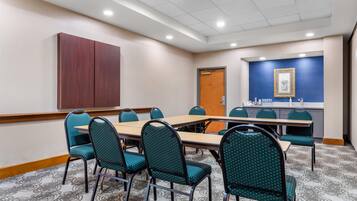 A conference room with a long table, multiple chairs, a wooden cabinet, a door, and a wall with a framed picture.