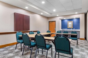A conference room with a long table, multiple chairs, a wooden cabinet, a door, and a wall with a framed picture. - Hampton Inn Guntersville (Guntersville)