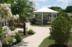 A gazebo with a white roof, surrounded by a pathway, benches, and greenery.