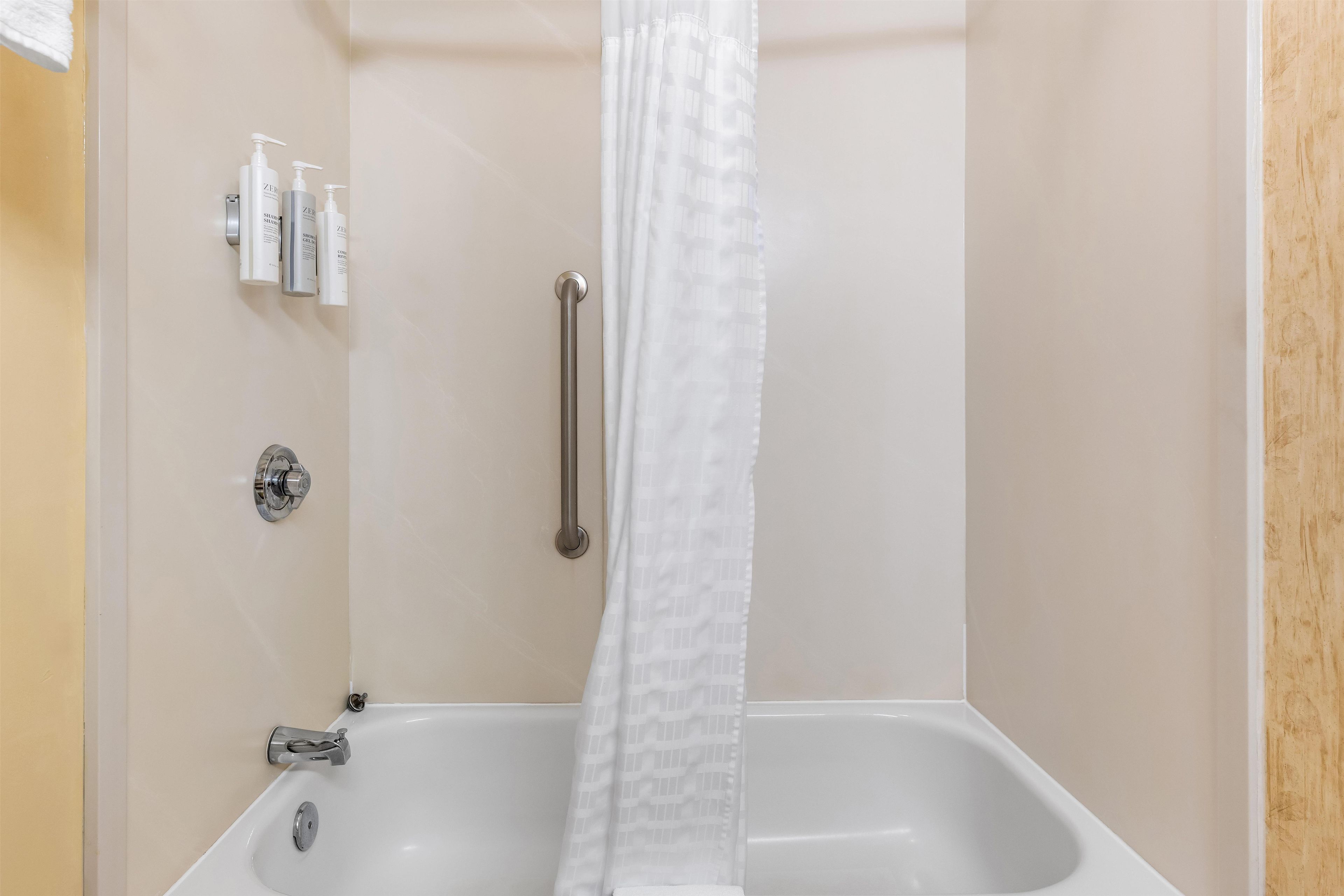 A bathroom with a bathtub, a shower curtain, and toiletries on the wall.