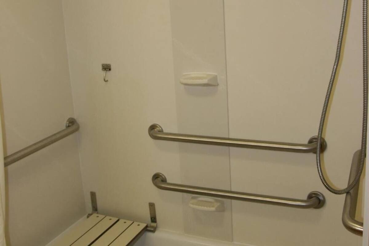 A shower area with a bench, grab bars, and a handheld showerhead.
