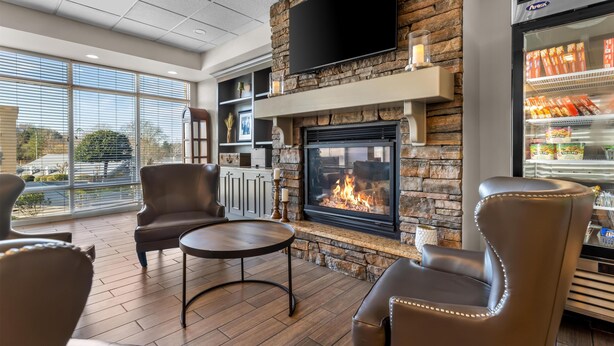 A modern lounge area with a stone fireplace, leather chairs, a flat-screen TV, and a beverage refrigerator. - Hampton Inn Guntersville (Guntersville)