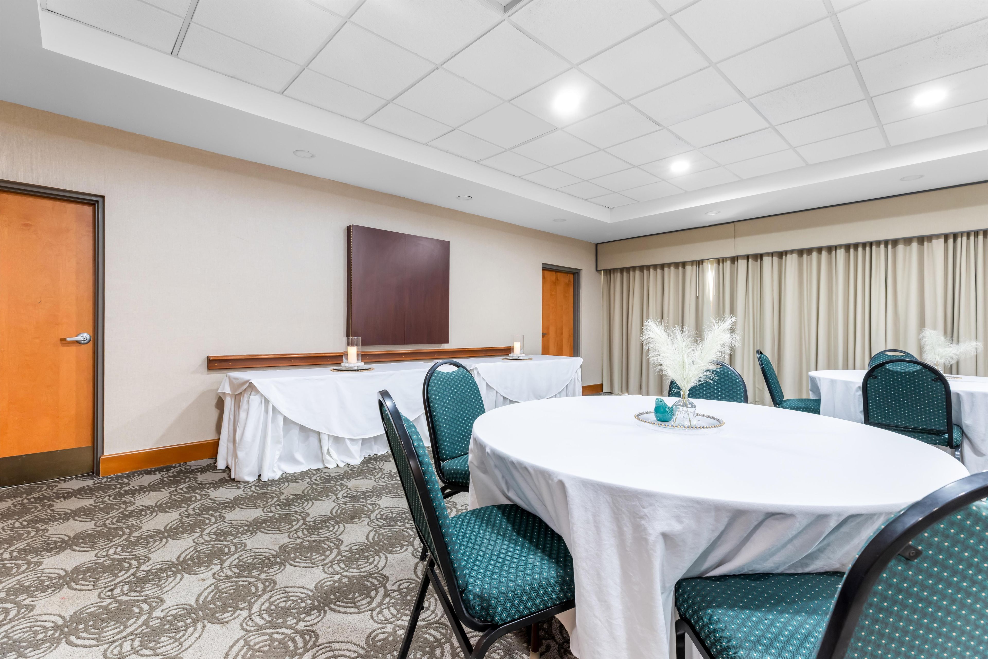 Un salón de conferencias con mesas redondas, sillas color turquesa y mantel blanco.