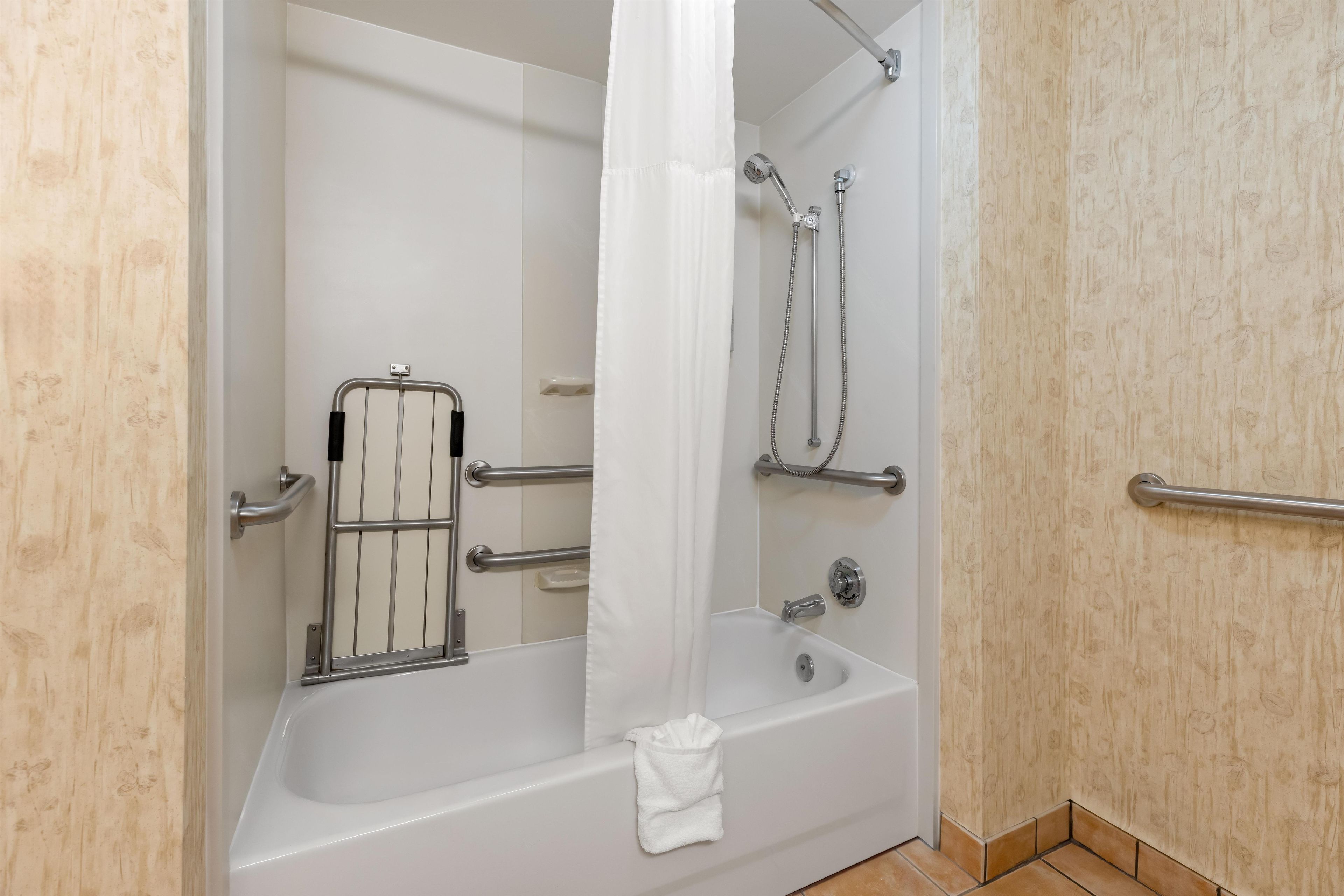Ein modernes Badezimmer mit Badewanne, Dusche und Haltegriffen.