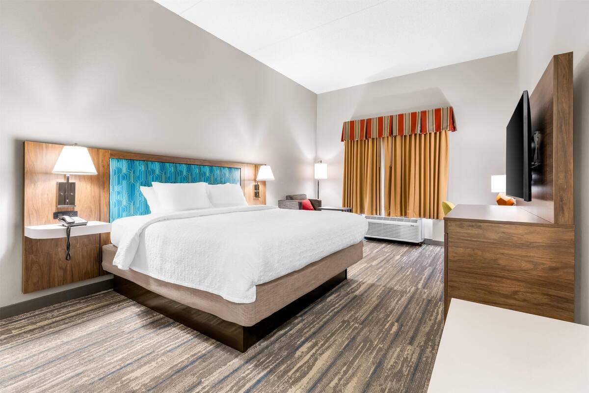 A hotel room with a large bed, bedside lamps, a flat-screen TV, a desk, and a window with curtains.