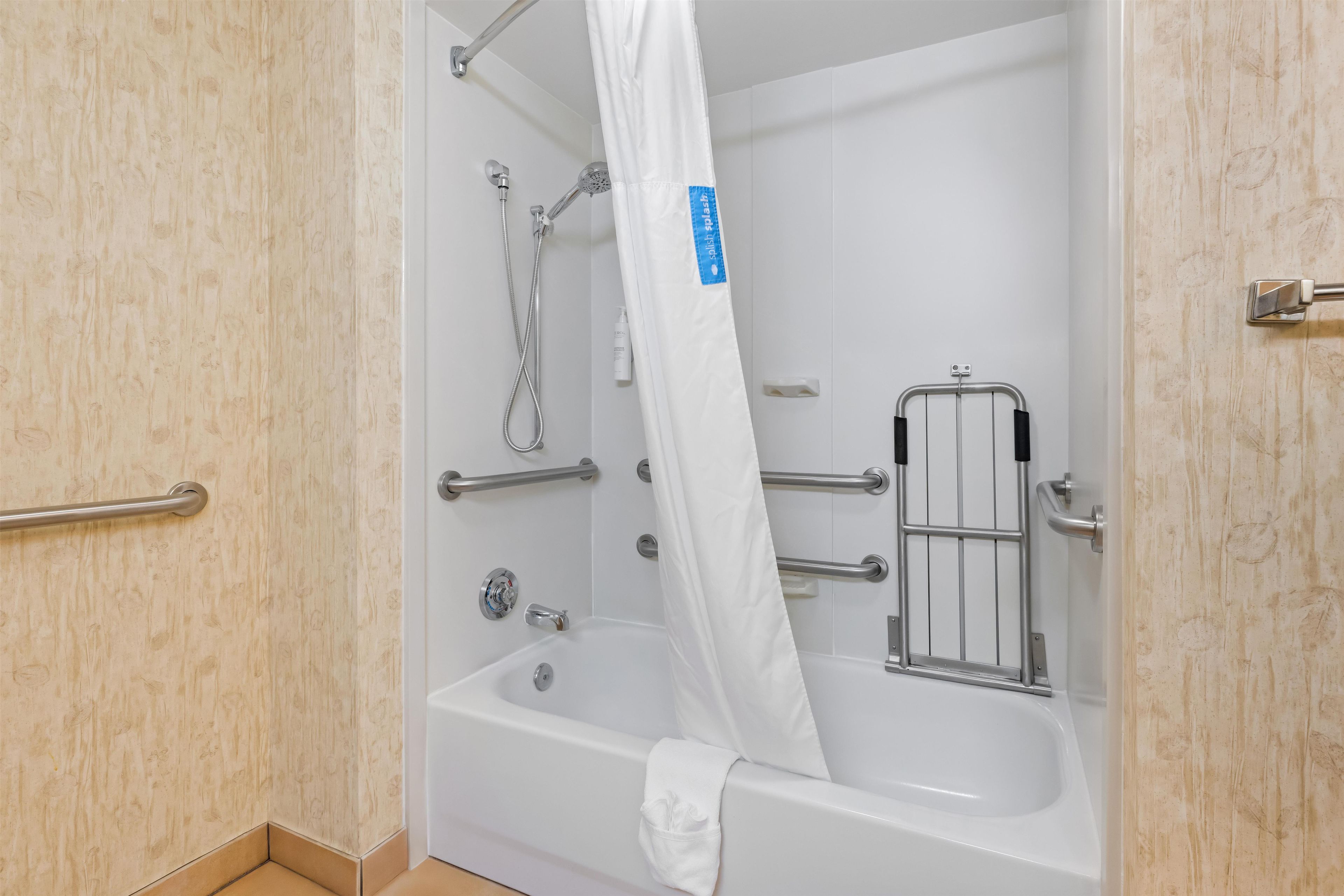 A bathroom with a bathtub, shower, grab bars, and a white curtain.