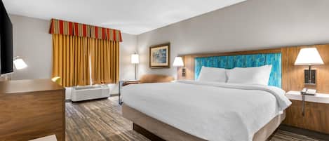 Ein Hotelzimmer mit einem großen Bett, einem Schreibtisch, einem Stuhl, einer Lampe, einem Gemälde und einem Telefon.