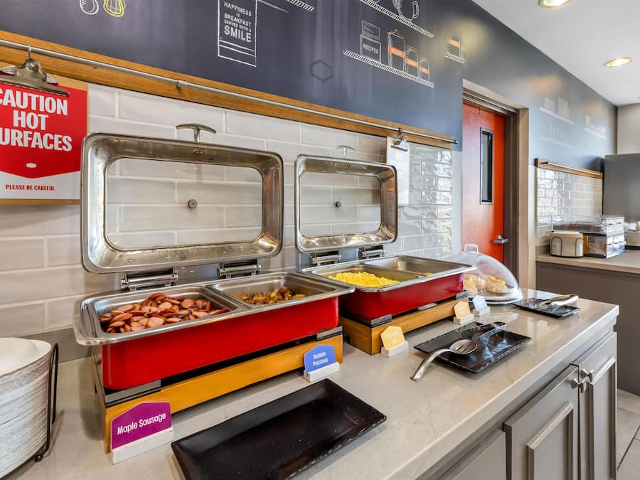 Un espace buffet avec différents stands de nourriture clairement identifiés, proposant notamment des saucisses à l’érable, des œufs brouillés et des pommes de terre rouges.