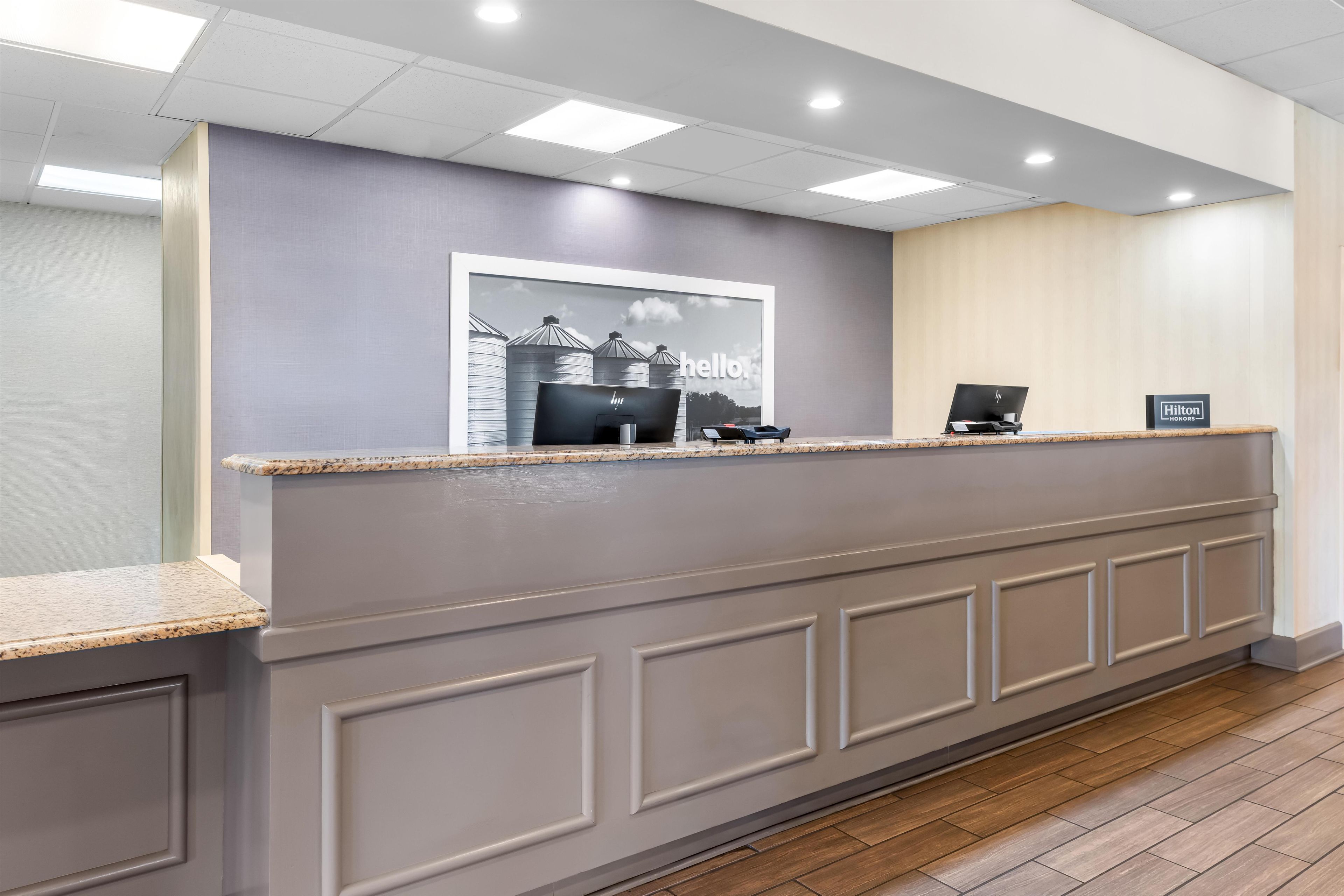 A hotel reception desk with a modern design, a framed welcome sign, and a computer.