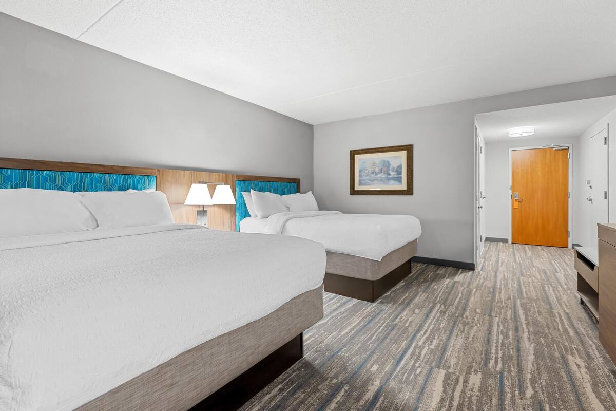 A hotel room with two beds, a wooden headboard, a framed picture on the wall, and a carpeted floor.