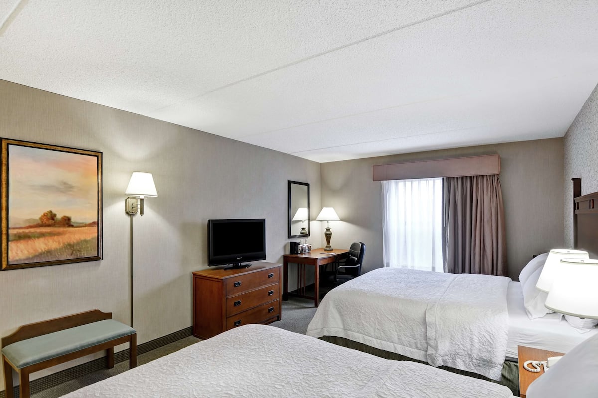 A hotel room with two beds, a desk with a television, a lamp, a chair, and a painting on the wall.