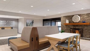 A hotel lobby with a reception desk, a seating area with a bench and chairs, a fireplace, and a clock on the wall. - Hampton Inn Bloomsburg (Bloomsburg)