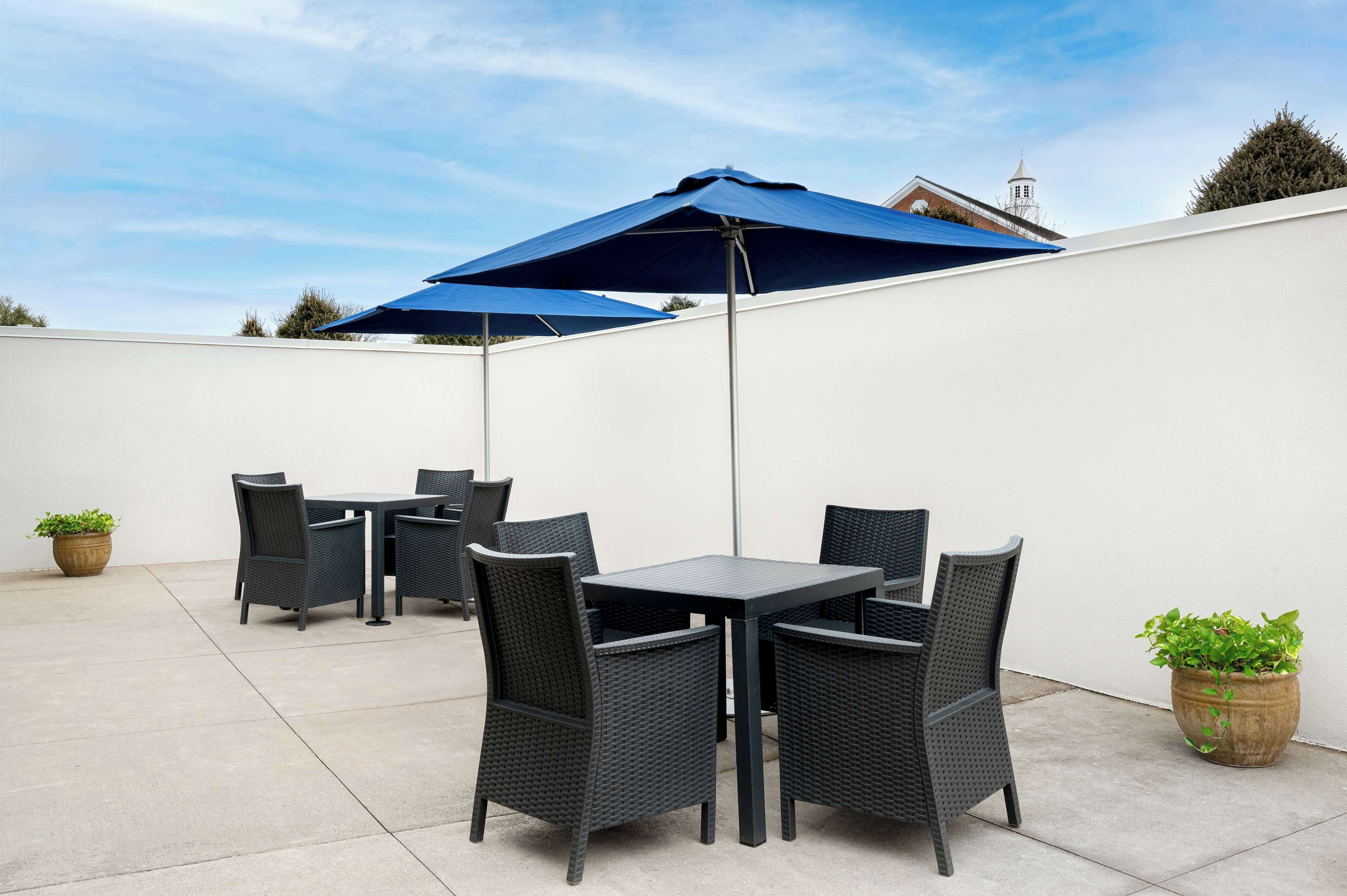 An outdoor patio with a table and chairs, a blue umbrella, and potted plants.