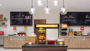 A breakfast area with a sign that reads "HAPPY BREAKFAST STARTS HERE," a fruit basket, and a juice dispenser. - Hampton Inn Bloomsburg (Bloomsburg)