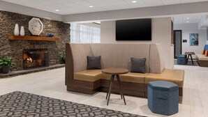 A modern lounge area with a stone fireplace, a large clock, and a flat-screen TV mounted on the wall. - Hampton Inn Bloomsburg (Bloomsburg)